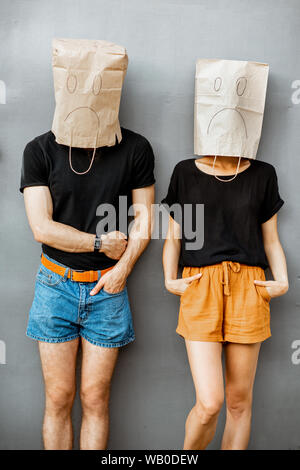 Portrait of a young couple with paper bags on their heads, standing together on the grey wall background Stock Photo