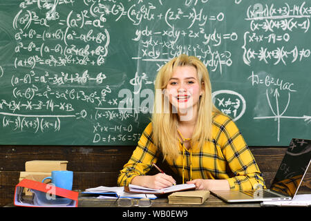 Attentive students writing something in their note pads while sitting at desks in the classroom. Students communicating during recess between lectures Stock Photo