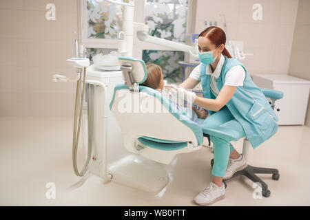 Red-haired child dentist wearing uniform examining girl Stock Photo