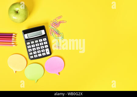 Math accessories for class. Flat lay of calculator, sticky notes and apple on yellow background. Stock Photo