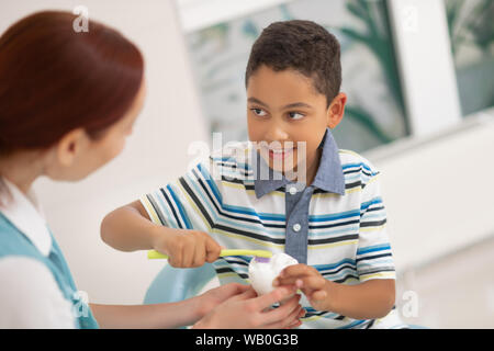 Boy smiling while talking to dentist and using tooth brush Stock Photo
