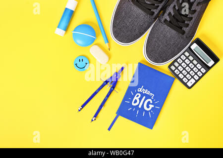 Top view of blue boy match school supplies, sneakers and a "Dream Big" notebook on yellow background. Stock Photo