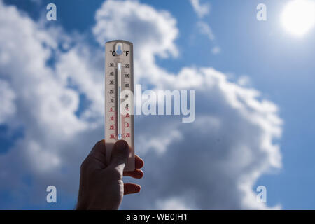Man keep thermometer in hand at sky with clouds background. Weather concept Stock Photo