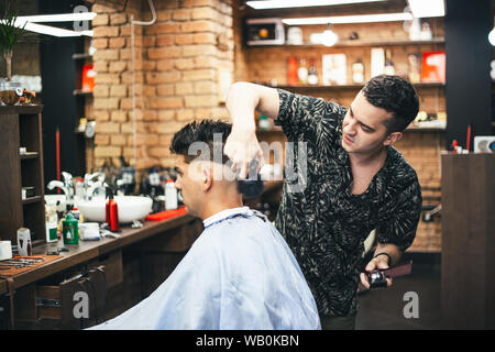 Bearded man with long beard, brutal, caucasian hipster with moustache, with stylish hair, haircut, getting powder on skin with makeup brush by barber Stock Photo
