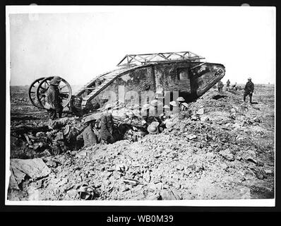 Tank moving across a battlefield at Thiepval, France. The tank appears to be moving over the top of a trench. In the trench there is a group of soldiers carefully watching it, they are all wearing steel helmets. There are also two soldiers standing next to the tank and some men visible further along the trench. The ground is extremely muddy and uneven, and strewn with debris.   The tank was developed and introduced by the British and French during World War I. It was first used at the Battle of the Somme on 15 September 1916, in a desperate bid to break the deadlock.  [Original reads: 'OFFICIA Stock Photo