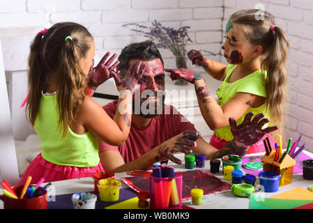 Creativity and imagination. Girls drawing on man face skin with colorful paints. Body art and painting. Fathers day and family concept. Daughters and Stock Photo