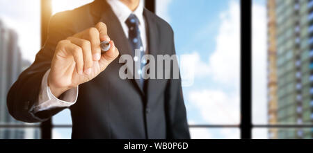 confident businessman hand holding black magic marker pen for write something , office work space with building for city background Stock Photo