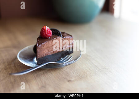 A piece of avocado chocolate vegan cake with oreo cookie and bright raspberry on top. Vegan desert. Stock Photo