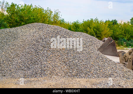 Yellow wheel loader bulldozer is working in quarry against the background of crushed stone storage. Stock Photo