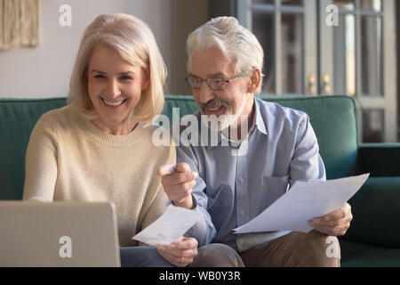 Happy old couple paying domestic bills online using computer app Stock Photo