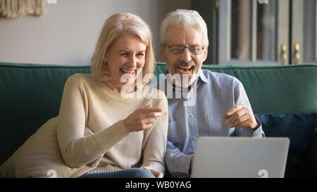 Happy old couple looking at laptop laughing watching comedy movie Stock Photo