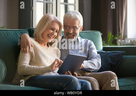 Happy senior old couple sit on sofa using digital tablet Stock Photo
