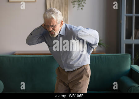 Upset senior man feeling back pain injury standing at home Stock Photo