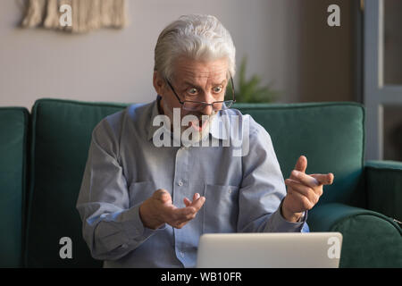 Shocked senior man looking at laptop reading unbelievable online news Stock Photo