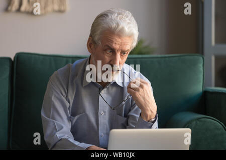 Puzzled serious thoughtful mature senior man looking at laptop screen Stock Photo