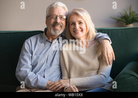 Happy senior couple bonding looking at camera sit on sofa Stock Photo