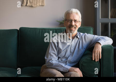 Smiling senior man sit on sofa in living room, portrait Stock Photo