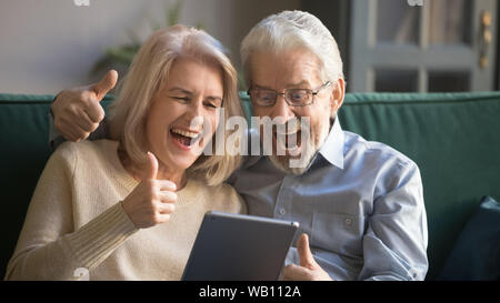 Excited senior couple looking at digital tablet show thumbs up Stock Photo