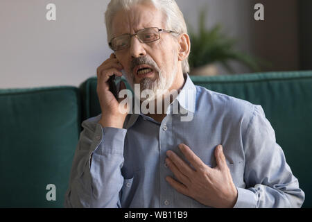 Senior man talking on phone calling 911 having heart attack Stock Photo