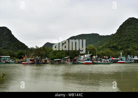 Fishing boats float in the water at the fishing village harbor with mountain in background at Ban Bangpu, Khao Sam Roi Yot, Thailand Stock Photo