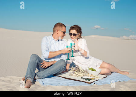 Young beautiful couple drinks a blue drink in a blue wine glass on a sand dune beach Stock Photo