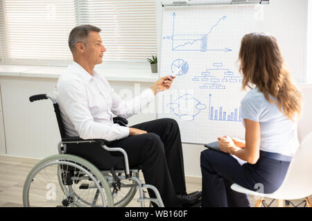 Disabled Matured Businessman Showing Diagram While Giving Presentation To His Colleague In Office Stock Photo
