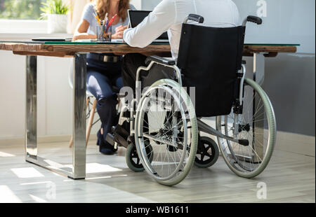 Rear View Of Disabled Businessman Working On Laptop With His Partner Stock Photo