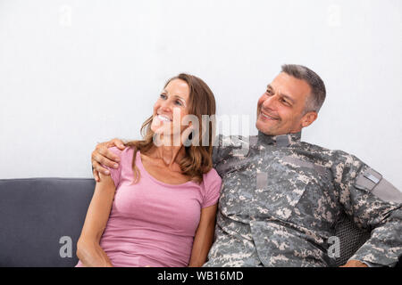 Happy Mature Army Man With His Loving Wife Sitting On Sofa Looking Away Stock Photo