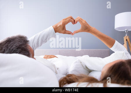 Rear View Of Couple Lying On Bed Making Heart Shape With Hands Stock Photo