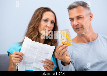 Matured Couple Sitting On Sofa Reading A Leaflet After Taking Pills At Home Stock Photo