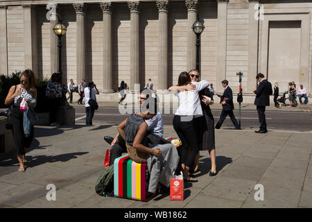 Two lady friends hug hello opposite the pillars of the Bank of England (right) at Bank triangle in the City of London, the capital's financial district (aka the Square Mile), on 22nd August 2019, in London, England. Stock Photo