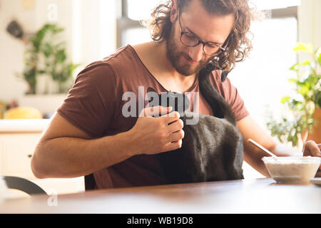 Young man stroking his black cat at home Stock Photo