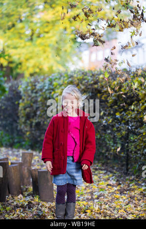 Portrait of grinning little girl throwing leaves in the air in autumn Stock Photo