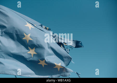 Torn EU flag wave on blue sky. European Union flag with twelve stars on sunny outdoor. Symbol of unity. Euro skepticism concept, copy space. Stock Photo