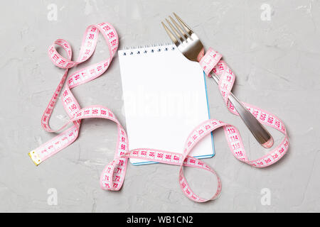 Pink measure tape, open notebook and fork on cement background with empty space for your idea. Top view of healthy lifestyle concept. Stock Photo