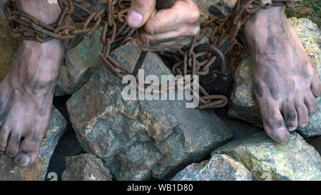 Hands and feet of a slave entangled in iron chains. An attempt to break free from slavery. The symbol of slave labor. Hands in chains Stock Photo