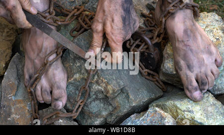 Hands and feet of a slave entangled in iron chains. An attempt to break free from slavery. The symbol of slave labor. Hands in chains Stock Photo