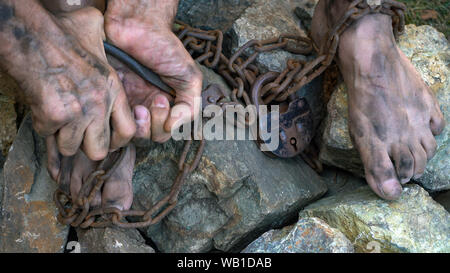 Hands and feet of a slave entangled in iron chains. An attempt to break free from slavery. The symbol of slave labor. Hands in chains Stock Photo