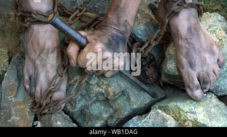 Hands and feet of a slave entangled in iron chains. An attempt to break free from slavery. The symbol of slave labor. Hands in chains Stock Photo