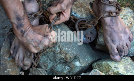 Hands and feet of a slave entangled in iron chains. An attempt to break free from slavery. The symbol of slave labor. Hands in chains Stock Photo