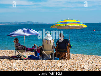 Lyme Regis, Dorset, UK. 23rd August 2019. UK Weather: People enjoy the sun under the shelter of a parasol at the seaside resort of Lyme Regis this afternoon. This weekend is set to be the hottest August Bank Holiday on record.  Credit: DWRAlamy Live News. Stock Photo