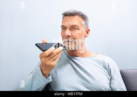 Close-up Of A Beard Man Using Voice Recognition Function On Mobile Phone Against White Background Stock Photo