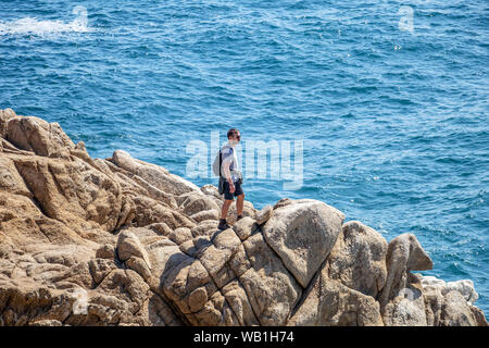 Young man brave hiker standing on the rocky coast of Pacific Ocean Stock Photo