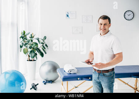smiling chiropractor holding Digital Tablet in hospital and looking at camera Stock Photo