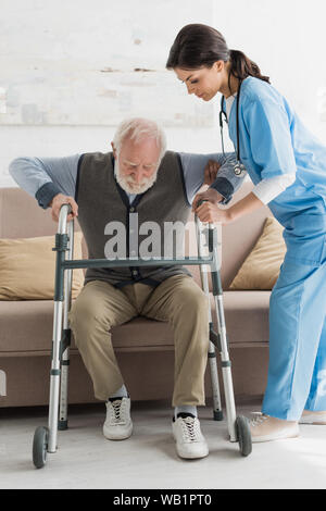 Nurse helping to retired man, getting up from sofa