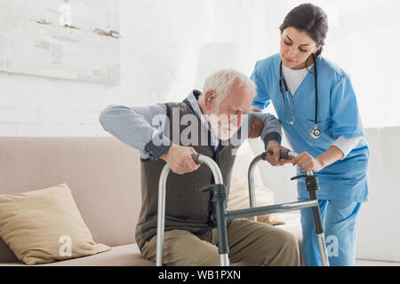 Doctor helping to retired man, getting up from sofa Stock Photo