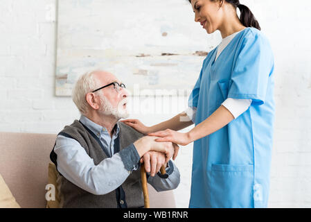 Side view of elderly man and nurse standing in room, looking at each other Stock Photo