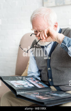 Upset grey haired man crying, and holding photo album in hands Stock Photo