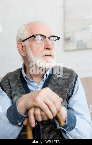 Calm and sad senior man with walking stick looking away, sitting in bright room Stock Photo
