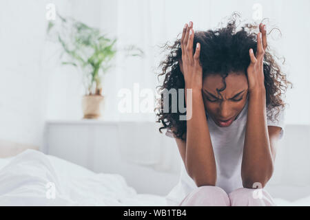 exhausted african american woman suffering from headache in bedroom Stock Photo